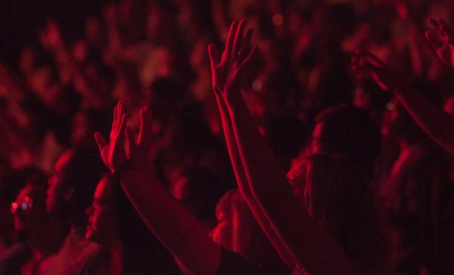 Crowd with hands raised in praise and illuminate by dark red light